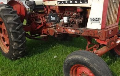 En röd och vit veteran-traktor av märket Farmall 504 på ett grönt gräsfält.