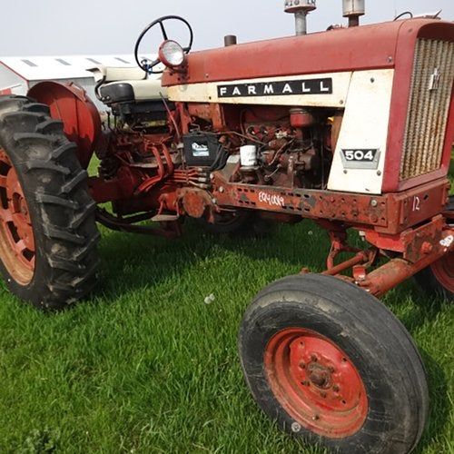 En röd och vit veteran-traktor av märket Farmall 504 på ett grönt gräsfält.